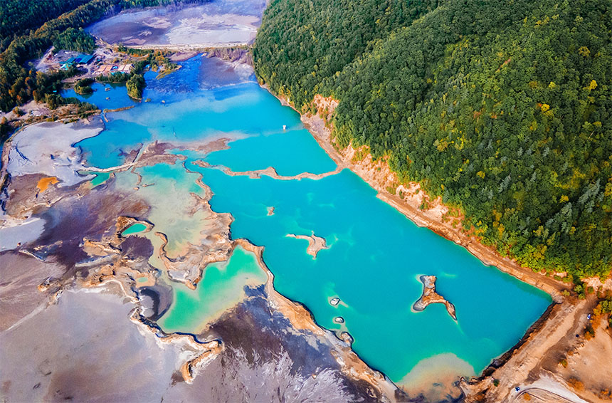 a tailings storage facility with blue water next to a green forest