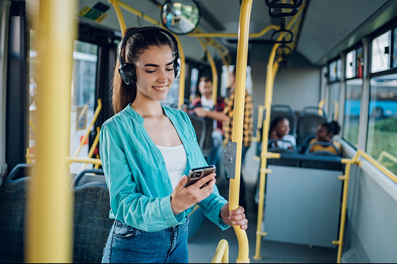 young woman on a bus smiling and using their mobile device