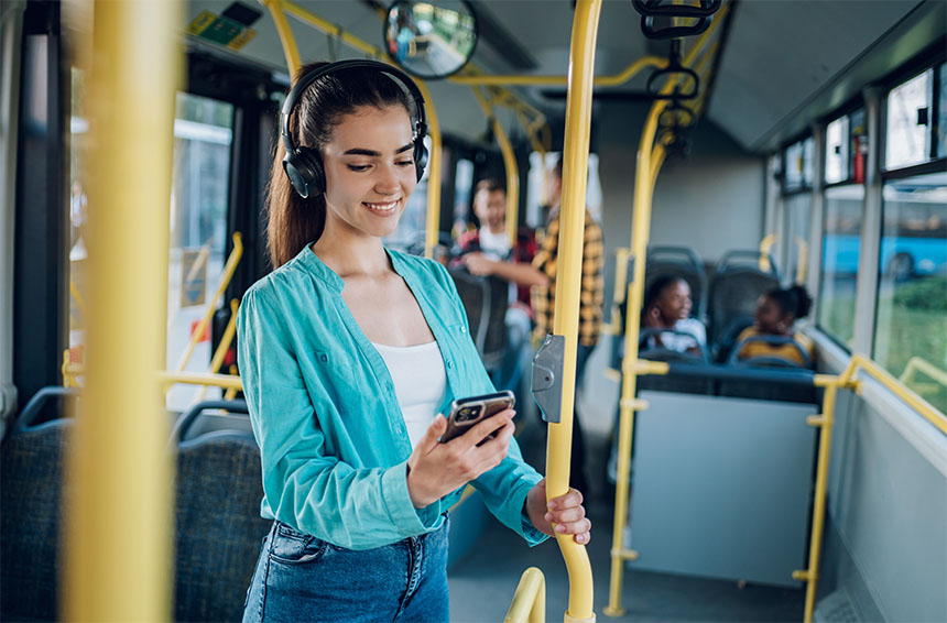 woman on bus wearing headphones while smiling and looking at her phone