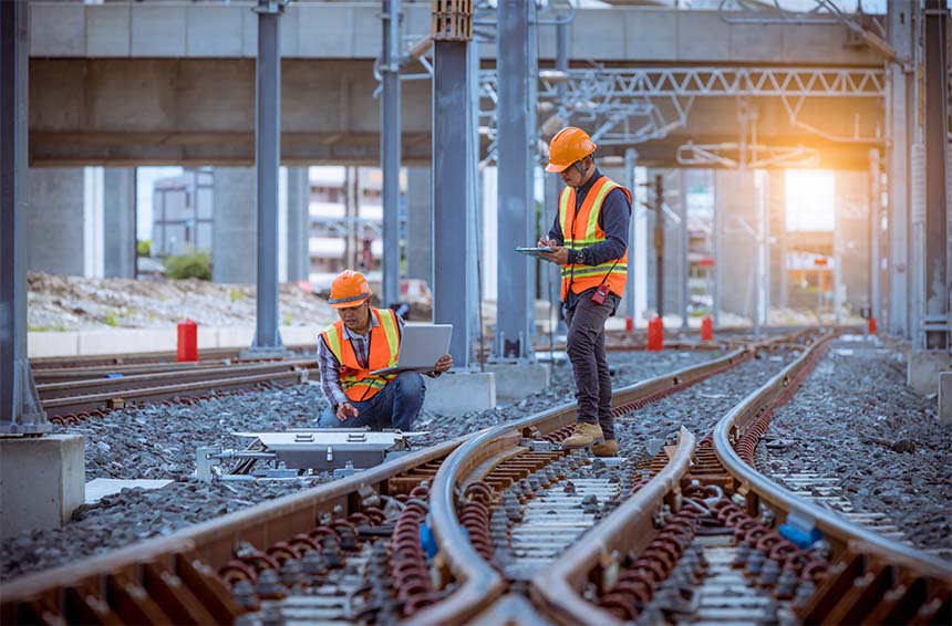 two engineers working on a rail line with laptops